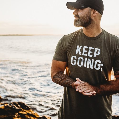 Photo of Kyle Poissonnier wearing a shirt that says "Keep Going". The ocean is in the background.