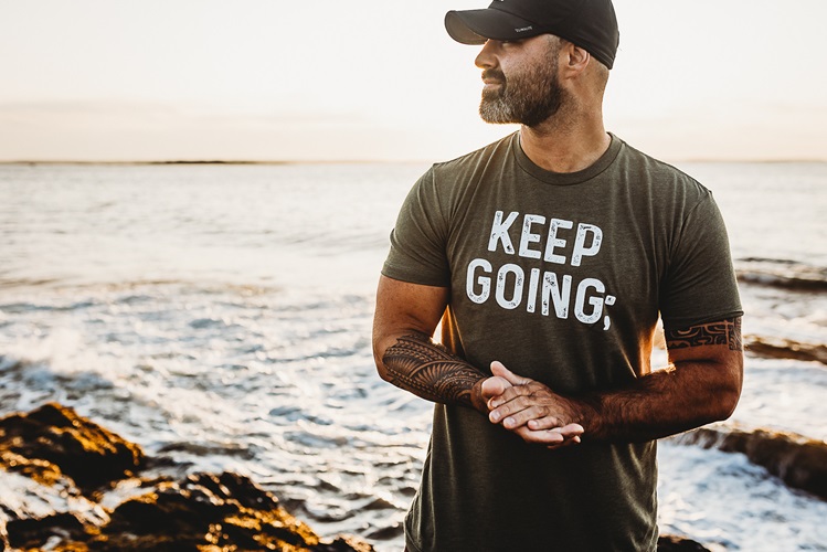 Photo of Kyle Poissonnier wearing a shirt that says "Keep Going". The ocean is in the background.