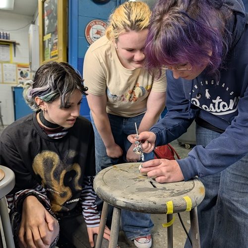 Photo of three students painting a 3-D model of Jupiter's moon Io.