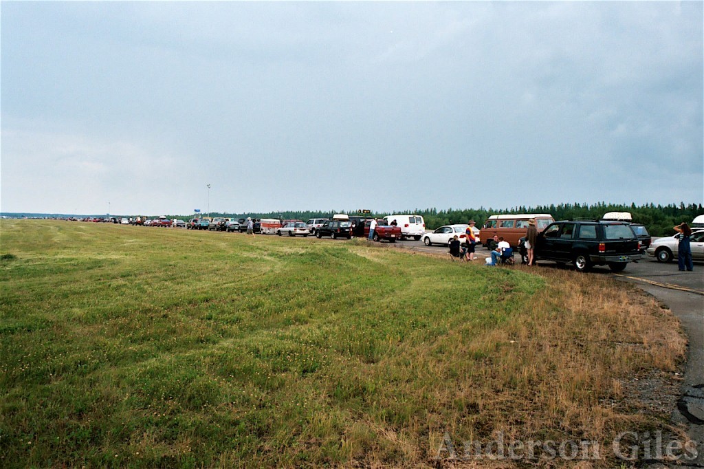 long line of cars next to a field