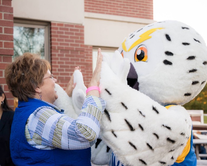 Photo of UMPI staff member high fiving Hootie the Owl mascot.