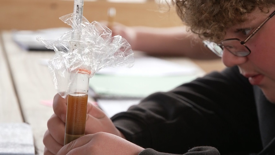 Video still from "Learning from Maine" episode--a student measures maple syrup in a beaker.