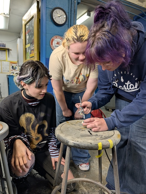 Photo of three students painting a 3-D model of Jupiter's moon Io.